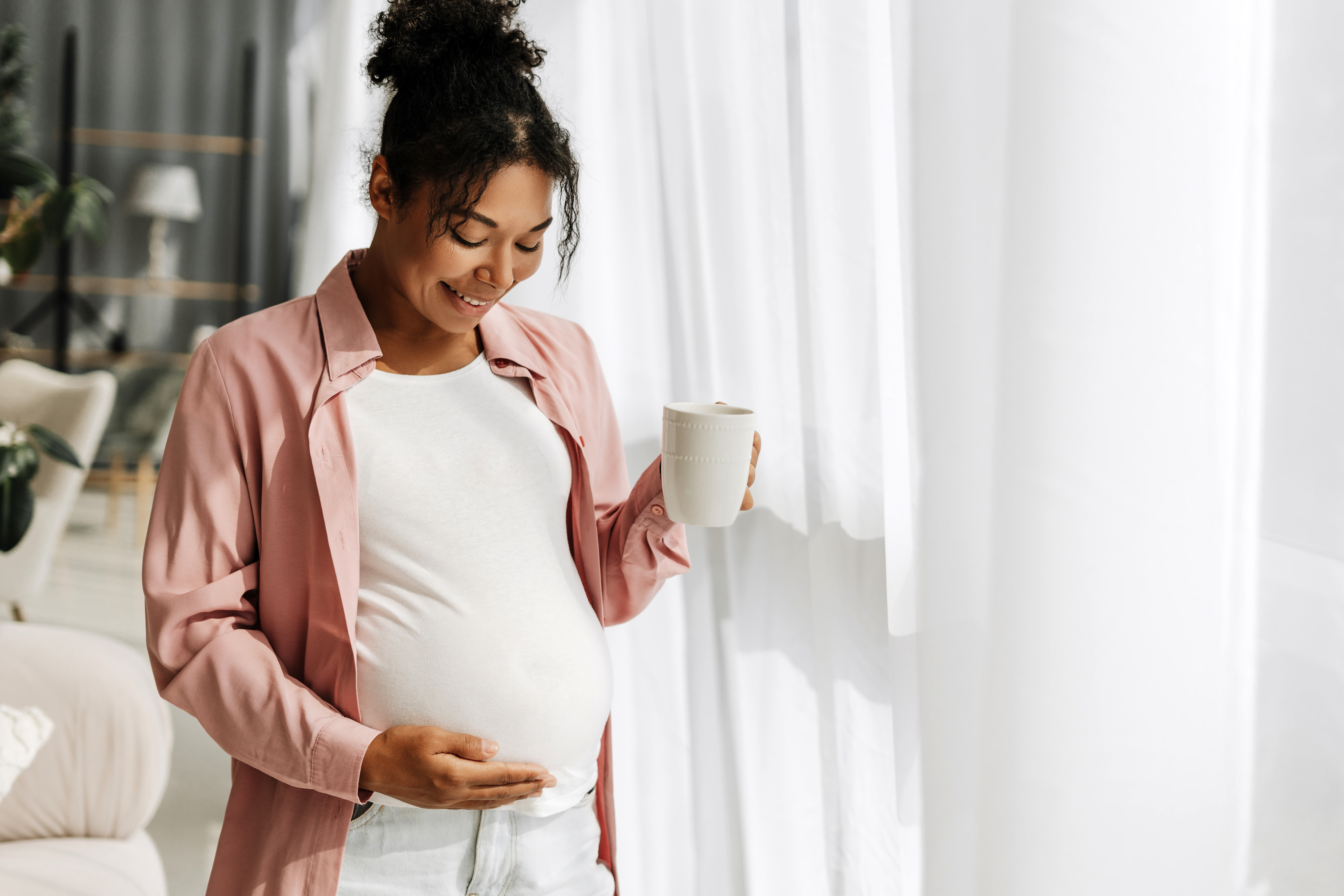 A woman in her third trimester, pausing quietly by the window